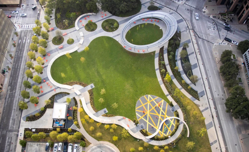 The park straight down: the lawn, the pavilion ring, the yellow-striped plaza and the curving walk around them, between downtown streets